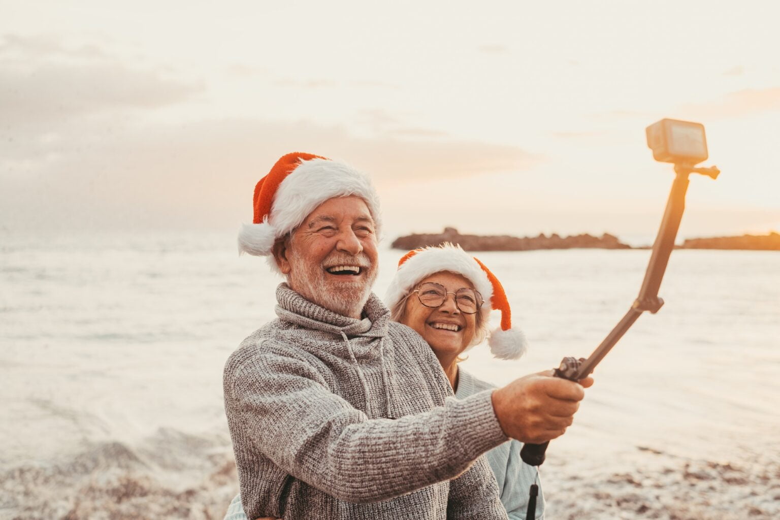 Portrait of two cute old persons having fun and enjoying together at the beach on christmas days